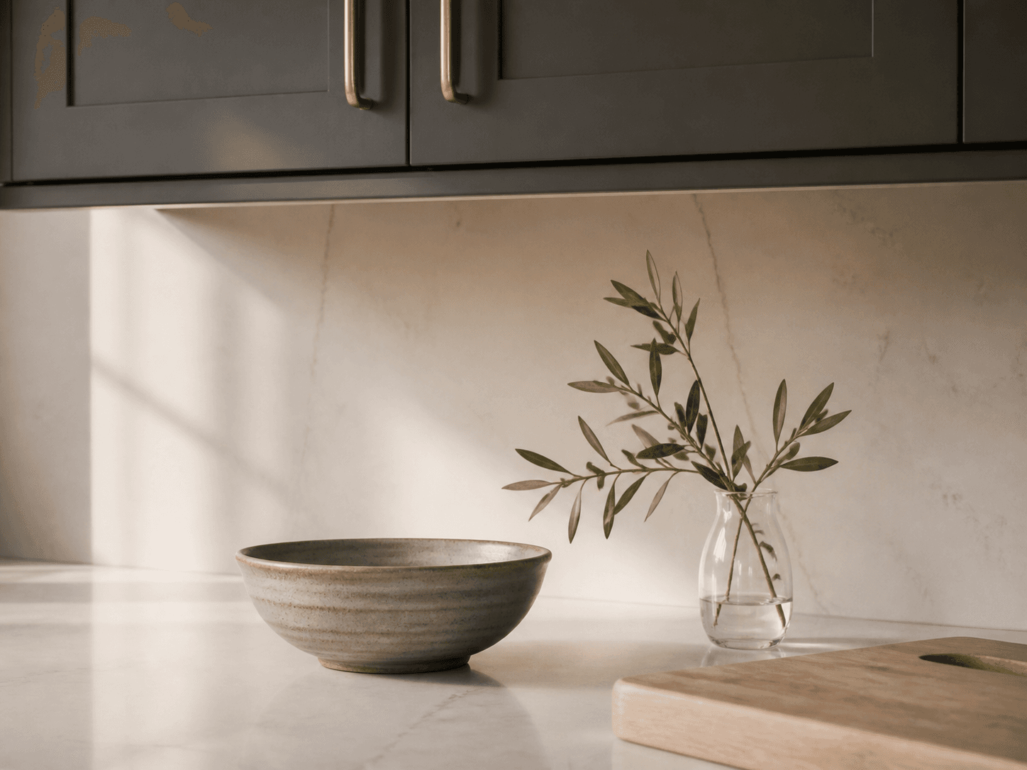 A ceramic bowl and an olive branch styled on a kitchen counter